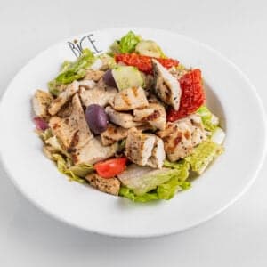 Grilled chicken salad with romaine lettuce, cherry tomatoes, red onions, cucumbers, olives, and house dressing