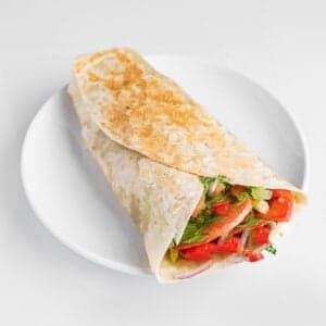 Veggie wrap with tortilla, provolone, roasted peppers, caramelized onions, eggplant, lettuce, and tomato
