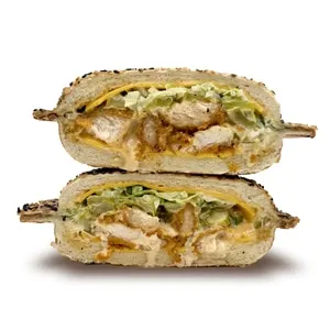 Fried chicken sandwich on a sesame panino bun with cheddar, Gold sauce, pickles, and lettuce