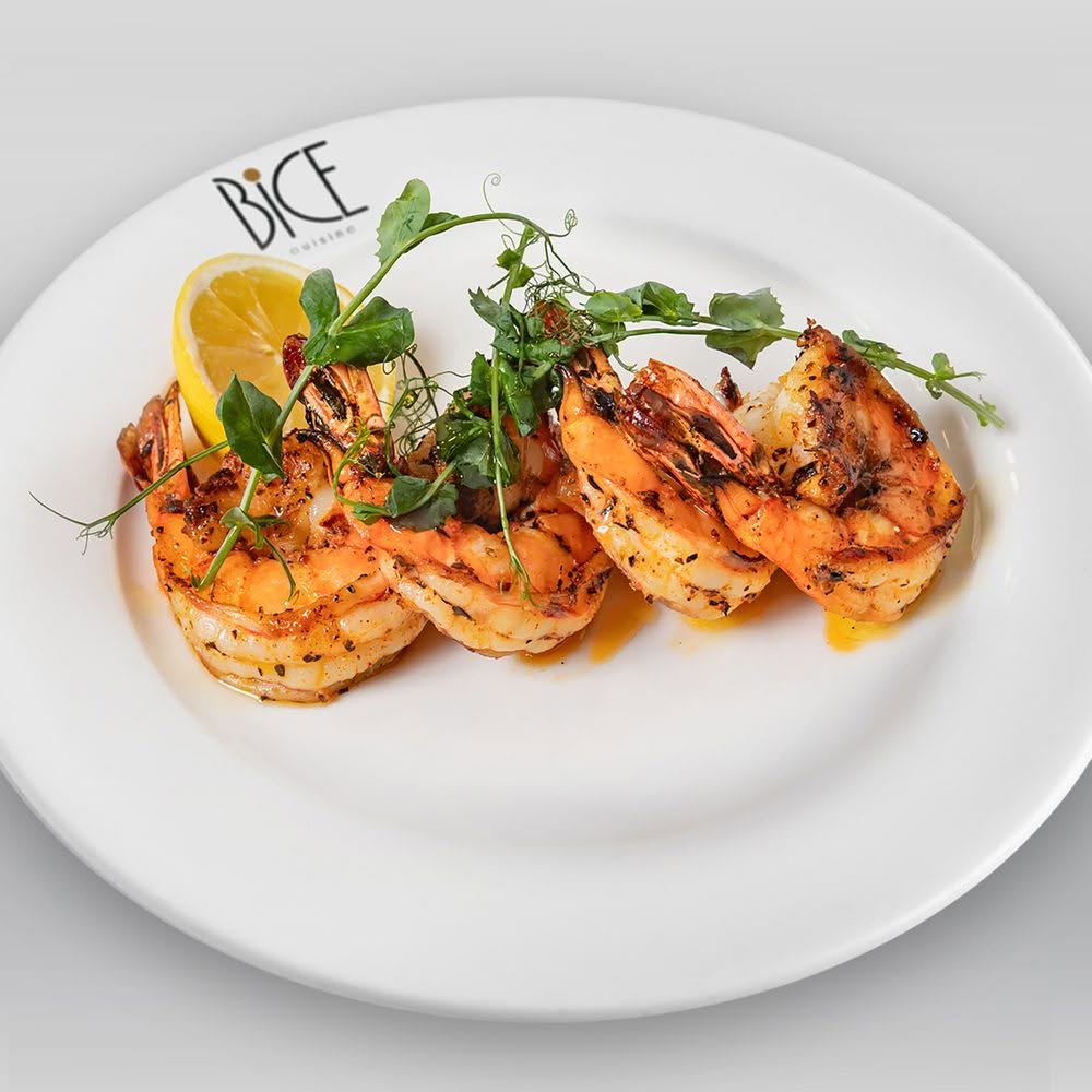 Crevettes grillées à la flamme, en sauce piri-piri, garnies d’herbes fraîches et de citron