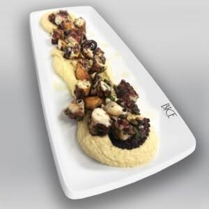 Pieuvre grillée au charbon sur houmous crémeux, garnie d’herbes fraîches et d’agrumes