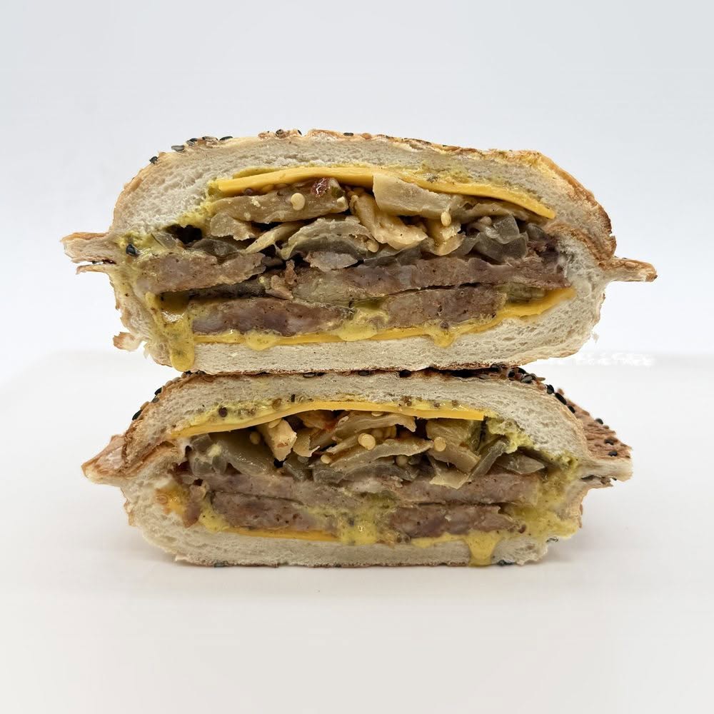 Saucisse italienne servie dans un pain panino au sésame avec cheddar, moutarde au miel, oignons caramélisés et aubergines